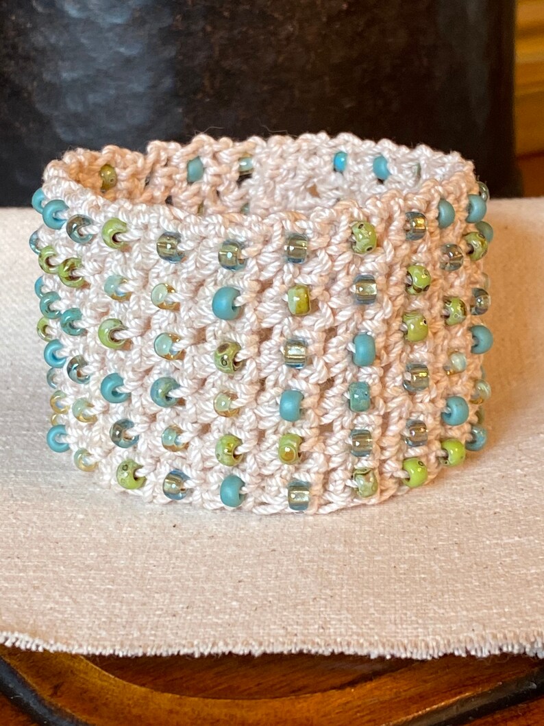 K&ouml;nnte beinhalten: Ein wei&szlig;es geh&auml;keltes Armband mit blauen, gr&uuml;nen und durchsichtigen Perlen.