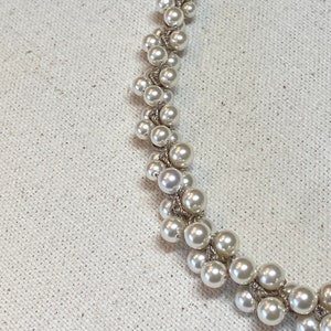 May include: A white pearl necklace with a delicate, interwoven design. The pearls are arranged in a cascading pattern, creating a unique and elegant look.