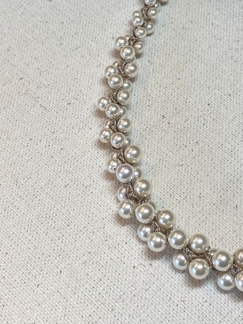 May include: A white pearl necklace with a delicate, interwoven design. The pearls are arranged in a cascading pattern, creating a unique and elegant look.
