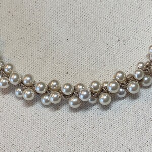 May include: A white pearl necklace with a silver chain. The pearls are clustered together in a random pattern.