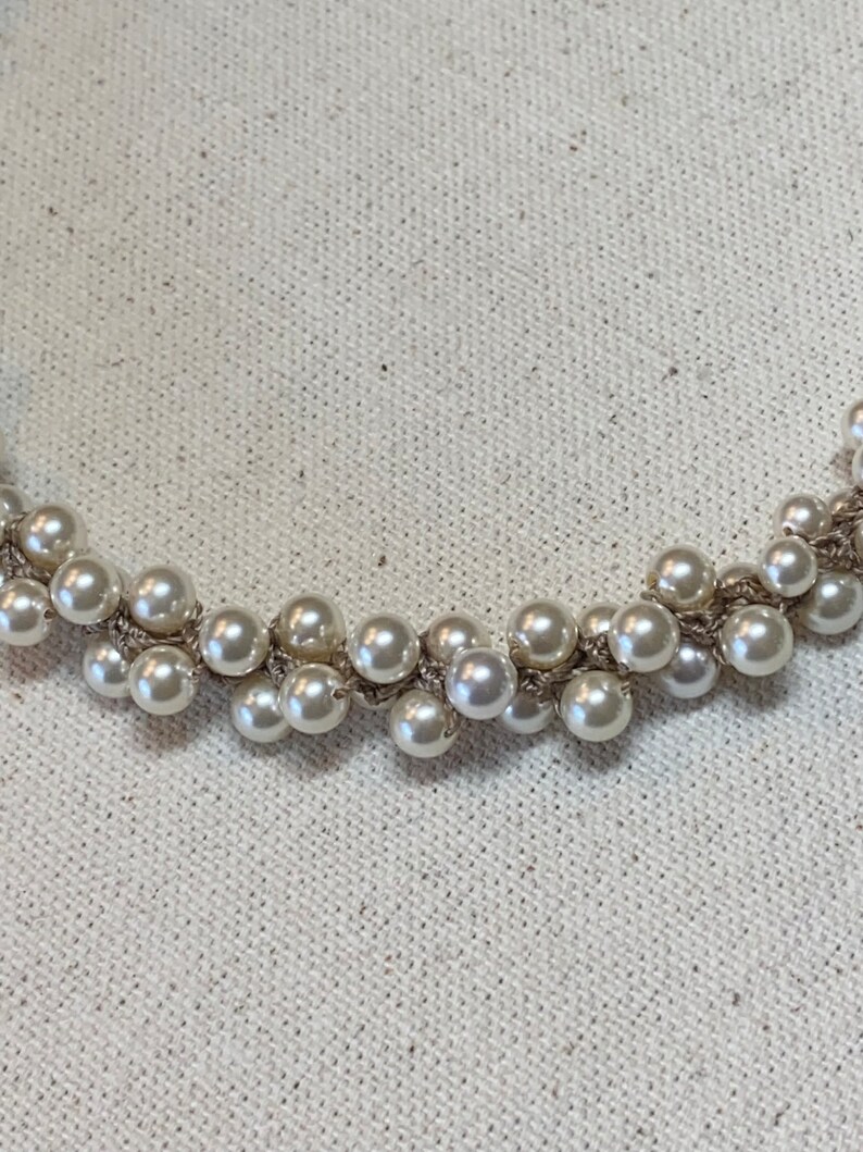 May include: A white pearl necklace with a silver chain. The pearls are clustered together in a random pattern.