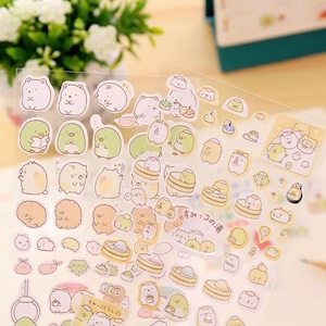 May include: A sheet of clear stickers featuring various cartoon characters in white, yellow, and green. The stickers depict bears, penguins, and other creatures in different poses and settings. Some stickers have Japanese text.