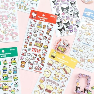 May include: A collection of colorful sticker sheets featuring various Sanrio characters like Hello Kitty, My Melody, and Keroppi. Each sheet is filled with themed stickers, including food items and character illustrations. The stickers are on a light pink background.