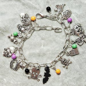 May include: A silver charm bracelet with Halloween themed charms, including skulls, bats, pumpkins, and a tombstone that says "RIP". The bracelet also has orange, green, and purple beads.