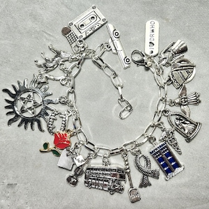 May include: Silver charm bracelet with various charms, including a cassette tape, a sunburst, a red rose, a London double-decker bus, and a blue police box. The bracelet has a lobster clasp closure.