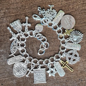 May include: A silver charm bracelet with various religious-themed charms. Charms include crosses, the word "Faith", "Jesus", "Blessed", and "Hope". Other charms include the words "Grace" and "Believe".