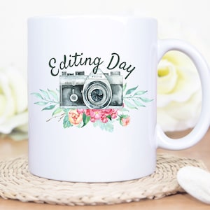 May include: White ceramic mug with the text "Editing Day" and a watercolor illustration of a vintage camera with pink flowers.