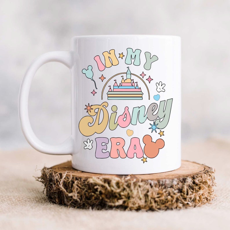 Op de afbeelding: Witte keramische mok met een kleurrijke afbeelding waarop "In My Disney Era" staat met een cartoonkasteel, Mickey Mouse-oren en sterren.