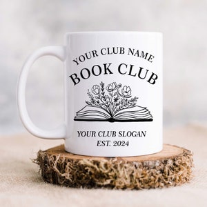 May include: White ceramic mug with a black design that says "Your Club Name Book Club" with a stylized open book with flowers coming out of it. Below the book is the text "Your Club Slogan Est. 2024".