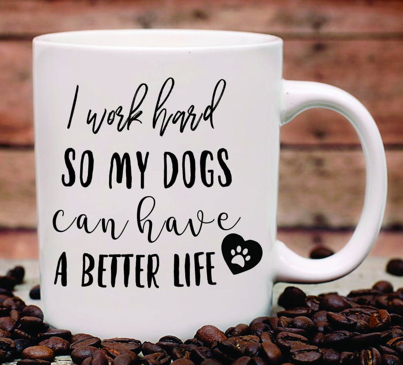 May include: White ceramic coffee mug with black text that reads "I work hard so my dogs can have a better life" with a black paw print inside a heart.