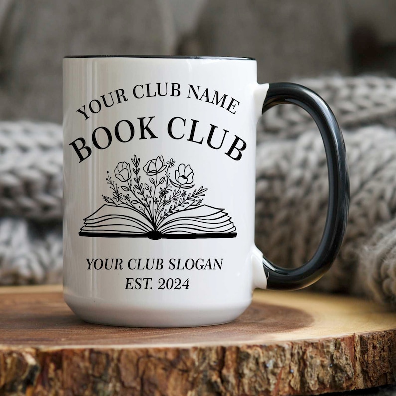May include: White ceramic mug with a black rim and handle. The mug has a black and white design of an open book with flowers and the text "YOUR CLUB NAME BOOK CLUB YOUR CLUB SLOGAN EST. 2024".