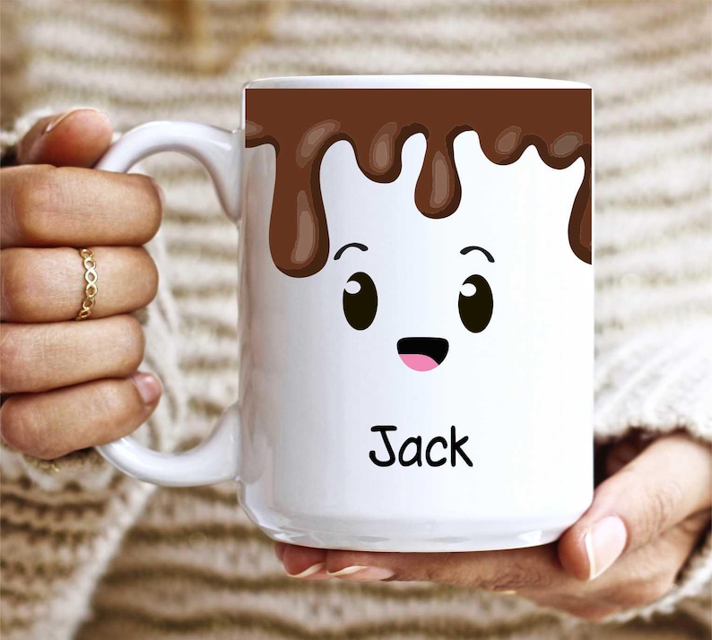 K&ouml;nnte beinhalten: Wei&szlig;e Keramik-Tasse mit einem Cartoon-Marshmallow-Design. Die Oberseite der Tasse zeigt ein braunes Schokoladen-Tropf-Design mit einem l&auml;chelnden Marshmallow-Gesicht darunter. Der Name "Jack" ist in schwarzer Schrift auf die Tasse gedruckt.