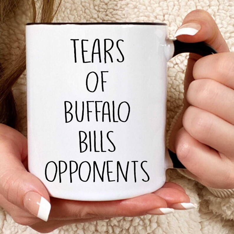May include: White ceramic coffee mug with a black rim and handle. The mug has black text that reads "Tears of Buffalo Bills Opponents".