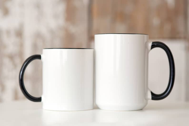 May include: Two white ceramic mugs with black handles and black rims. The mugs are empty and sitting on a white surface.