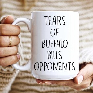 May include: White ceramic coffee mug with black text that reads "Tears of Buffalo Bills Opponents".