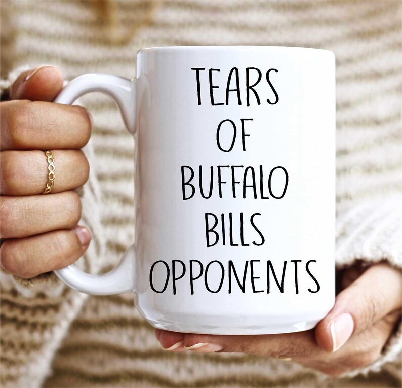 May include: White ceramic coffee mug with black text that reads "Tears of Buffalo Bills Opponents".