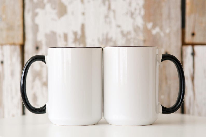 May include: Two white ceramic mugs with black handles and a black rim. The mugs are empty and sitting on a white surface.