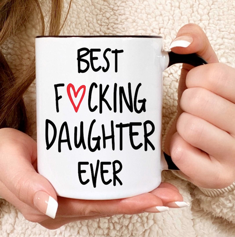 May include: White ceramic coffee mug with a black handle. The mug has black text that reads "BEST F♡CKING DAUGHTER EVER".