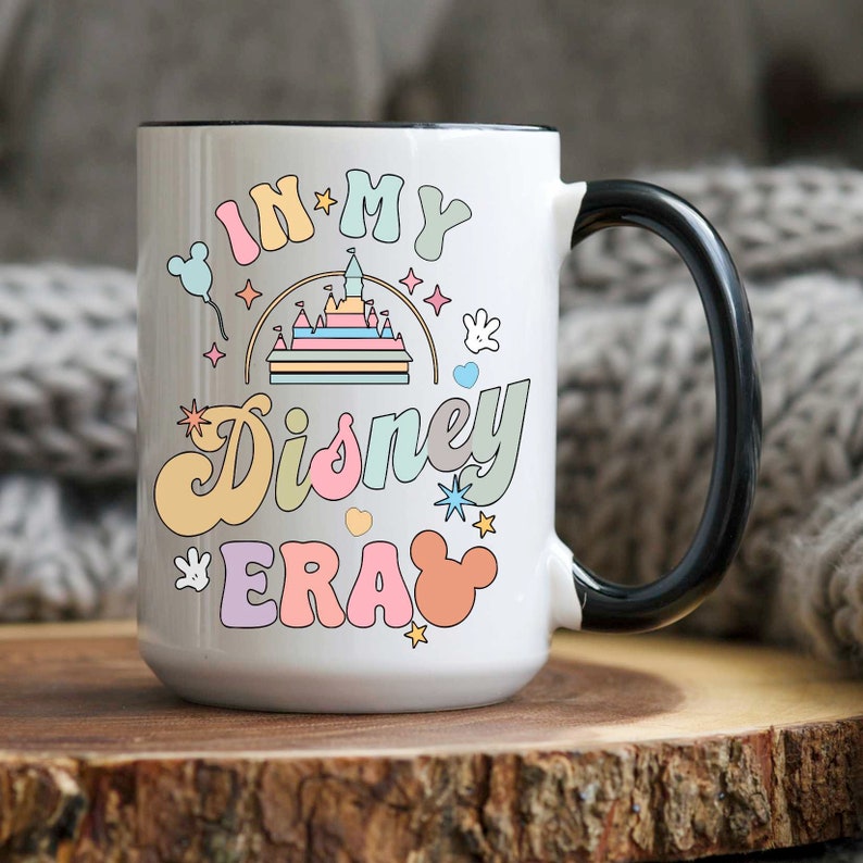 Op de afbeelding: Witte keramische mok met een zwart handvat. De mok heeft een kleurrijke afbeelding met de tekst "In My Disney Era" met een cartoonkasteel, sterren en Mickey Mouse-oren.