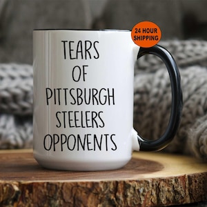 K&ouml;nnte beinhalten: Wei&szlig;e Keramik-Kaffeetasse mit schwarzem Henkel und schwarzem Rand. Die Tasse tr&auml;gt den Text "Tears of Pittsburgh Steelers Opponents" in schwarzer Schrift.