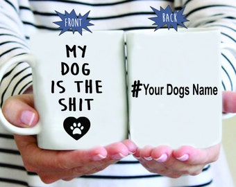 May include: White ceramic coffee mug with black text that reads "My Dog Is The Shit" with a paw print inside a heart. The back of the mug has the text "#Your Dogs Name".