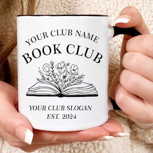 May include: White ceramic mug with a black rim and handle. The mug has a black and white design of an open book with flowers coming out of it. The text "YOUR CLUB NAME BOOK CLUB YOUR CLUB SLOGAN EST. 2024" is printed on the mug.
