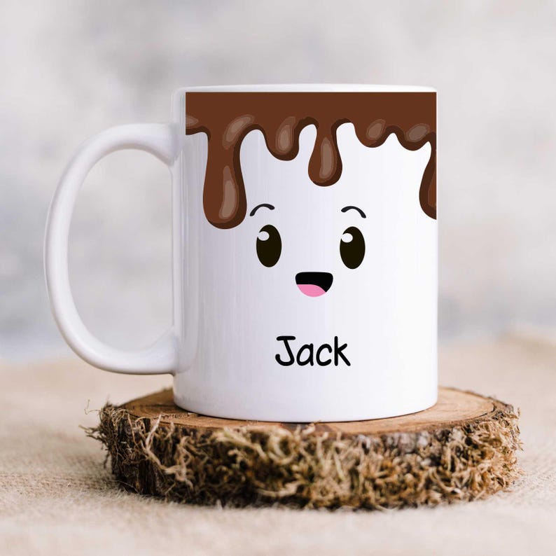 K&ouml;nnte beinhalten: Wei&szlig;e Keramik-Tasse mit einem Cartoon-Marshmallow-Gesicht. Die Tasse hat ein braunes Schokoladen-Tropf-Design oben, mit dem Namen "Jack" in Schwarz darunter gedruckt. Die Tasse steht auf einem Holzuntersetzer.