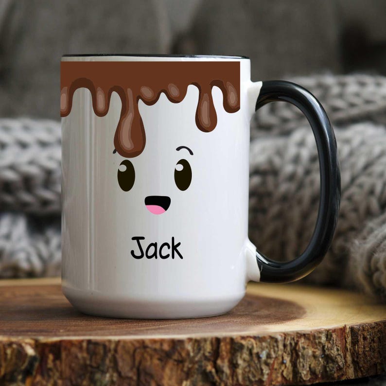 K&ouml;nnte beinhalten: Wei&szlig;er Keramikbecher mit schwarzem Griff und Rand, mit einem Cartoon-Gesicht mit brauner Schokolade, die von oben tropft. Der Name "Jack" ist unten auf dem Becher in Schwarz aufgedruckt.