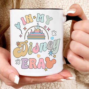 Op de afbeelding: Een witte keramische mok met een zwart handvat. De mok heeft een kleurrijk ontwerp met de tekst "In My Disney Era" en een cartoonafbeelding van Assepoester's kasteel.