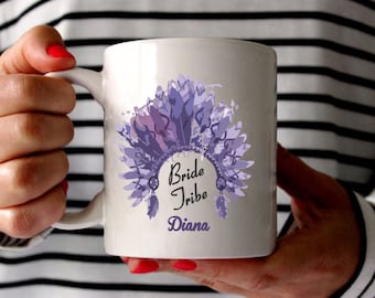 Könnte beinhalten: Weiße Keramiktasse mit einem lila und rosa Aquarelldesign eines Kopfschmucks mit Federn. Der Text "Bride Tribe Diana" ist auf die Tasse gedruckt.