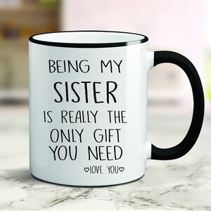May include: White ceramic coffee mug with a black rim and handle. The mug has black text that reads "Being my sister is really the only gift you need. Love you."