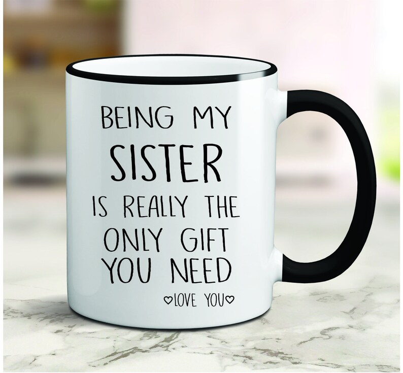 May include: White ceramic coffee mug with a black rim and handle. The mug has black text that reads "Being my sister is really the only gift you need. Love you."