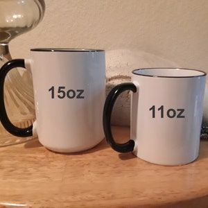 May include: Two white ceramic mugs with black handles and black rims. The larger mug is 15oz and the smaller mug is 11oz.