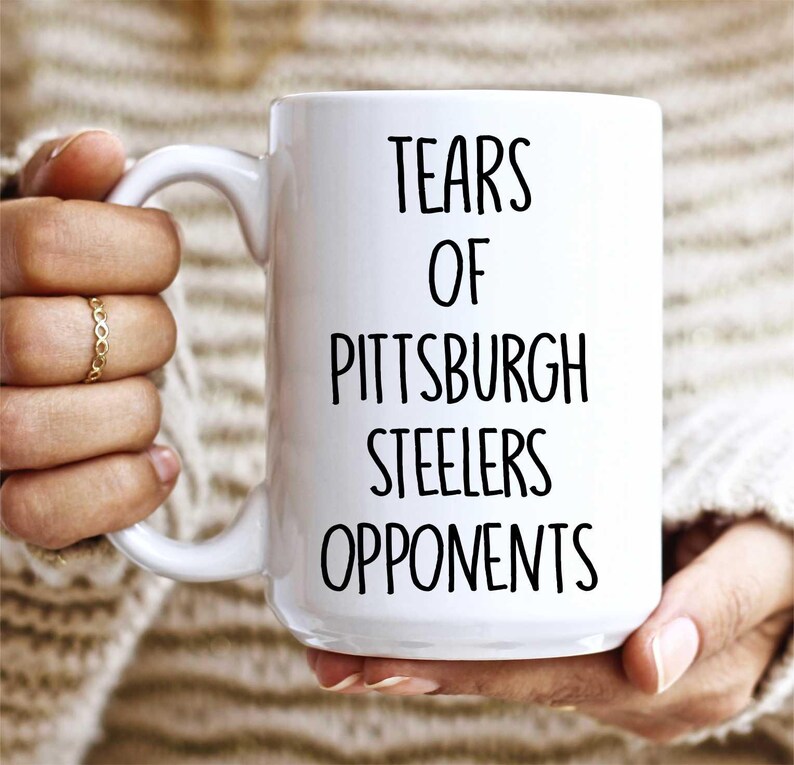 K&ouml;nnte beinhalten: Wei&szlig;e Keramik-Kaffeetasse mit schwarzem Text, der "Tears of Pittsburgh Steelers Opponents" lautet.