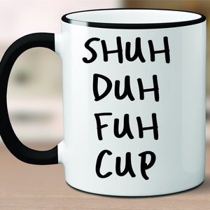 May include: White ceramic coffee mug with a black rim and handle. The mug has black text that reads "SHUH DUH FUH CUP".