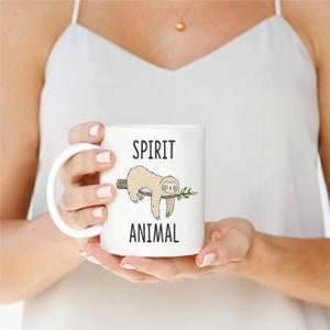 May include: White ceramic mug with a black and white illustration of a sloth hanging from a branch. The text "SPIRIT ANIMAL" is printed on the mug.