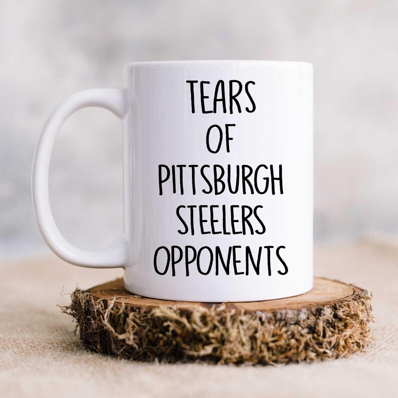 K&ouml;nnte beinhalten: Eine wei&szlig;e Keramik-Kaffeetasse mit schwarzem Text, der "Tears of Pittsburgh Steelers Opponents" lautet.