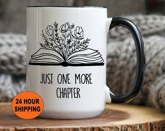 Puede incluir: Taza de cerámica blanca con asa y borde negros. La taza presenta una ilustración en blanco y negro de un libro abierto con flores que crecen de él. El texto "Just One More Chapter" está impreso debajo de la ilustración.