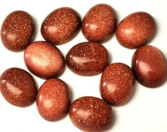 May include: A collection of eleven oval-shaped, polished gemstones. The stones are a deep reddish-brown color with a sparkling, glittery appearance. The gemstones are arranged on a white surface.