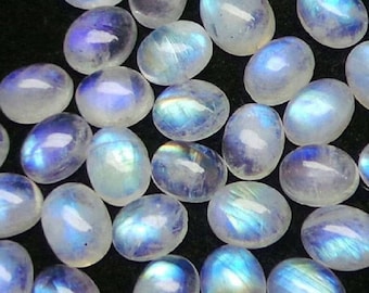 May include: A collection of oval-shaped moonstone cabochons. The stones display a milky white base with iridescent blue and rainbow flashes. The gemstones are smooth and polished, perfect for jewelry making or collecting.