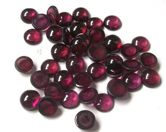 Pode incluir: Uma coleção de pedras preciosas redondas, lapidadas em cabochão, de cor vermelha. As pedras preciosas são lisas e polidas, com um acabamento brilhante.