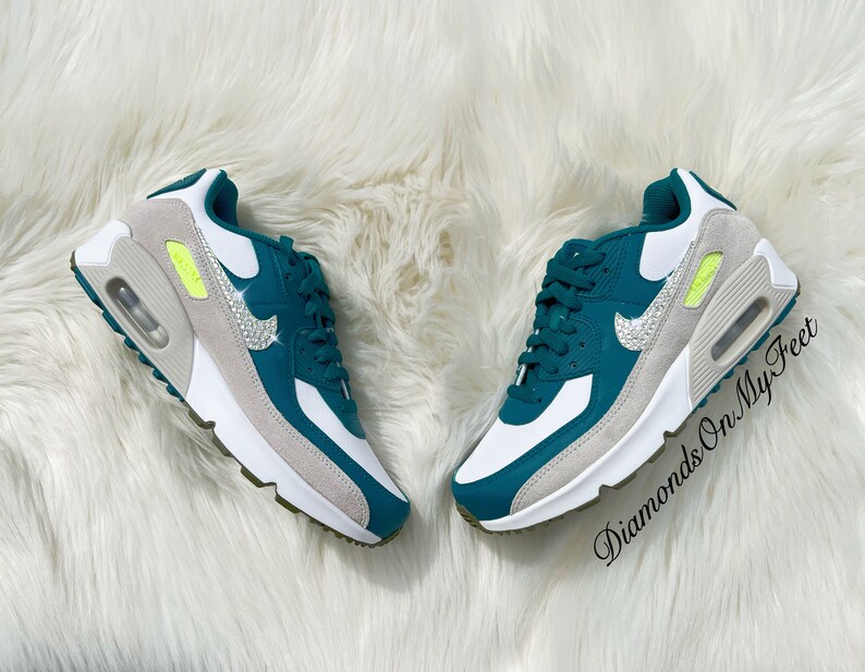 Puede incluir: Zapatillas de deporte de color azul verdoso y blanco con un swoosh blanco y diamantes de imitaci&oacute;n. Las zapatillas tienen una entresuela blanca y una suela gris. El texto "Diamonds On My Feet" es visible en la imagen.