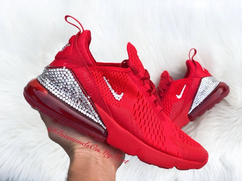 May include: Red Nike Air Max 270 sneakers with a white swoosh logo and a clear crystal embellishment on the heel. The sneakers have a red mesh upper and a white rubber sole.