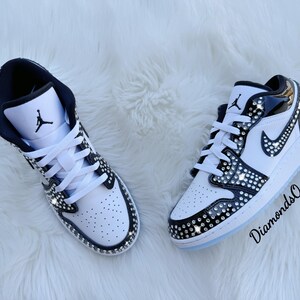May include: Pair of white and black sneakers with crystal embellishments. The shoes feature a black Nike swoosh and the Jumpman logo. The text "DiamondsOnMyFeet" is visible on the right shoe.