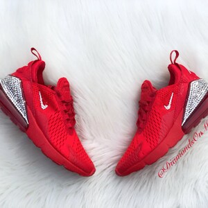 May include: Red Nike Air Max 270 sneakers with a white swoosh logo and a clear crystal-encrusted heel. The shoes are on a white fluffy surface. @DiamondsOnMyFeet