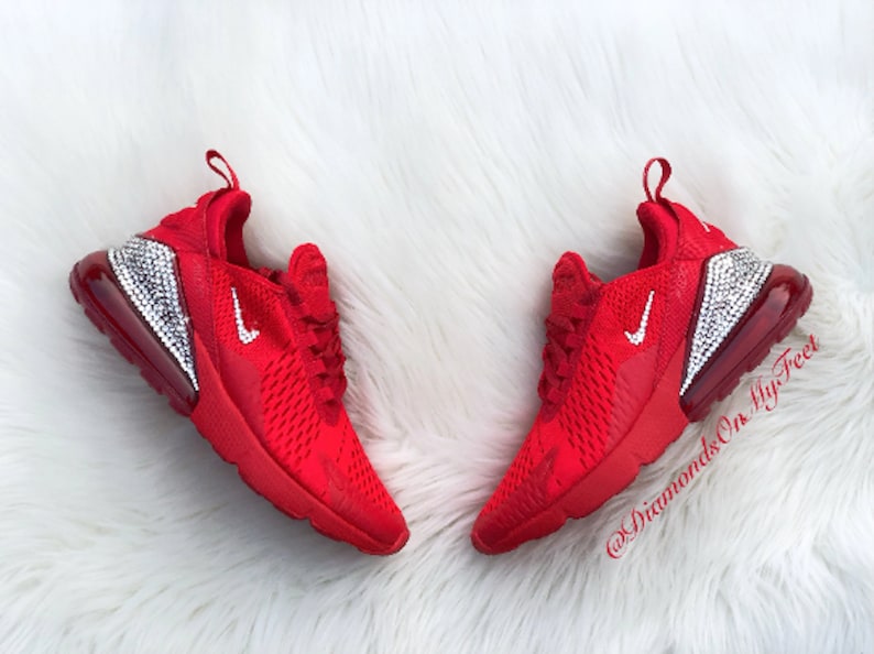 May include: Red Nike Air Max 270 sneakers with a white swoosh logo and a clear crystal-encrusted heel. The shoes are on a white fluffy surface. @DiamondsOnMyFeet