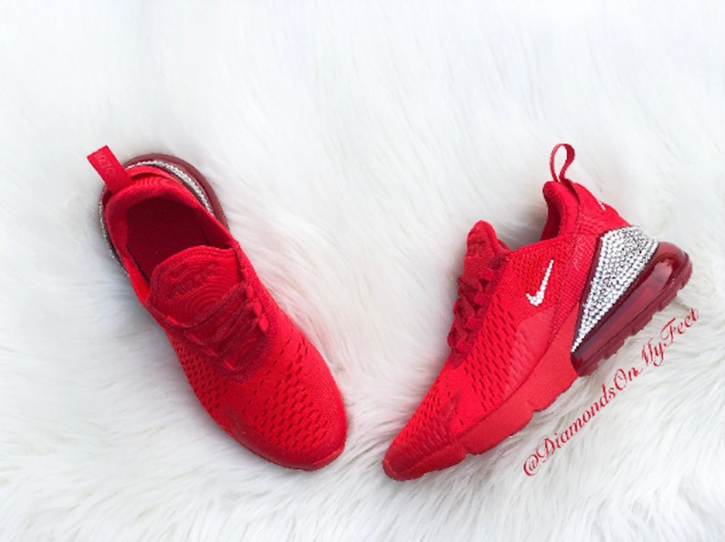 May include: Red Nike Air Max 270 sneakers with a white swoosh and a clear crystal-encrusted heel. The shoes are on a white fluffy surface. @DiamondsOnMyFeet