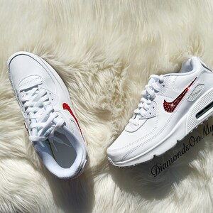 May include: White leather sneakers with a red jeweled swoosh logo. The text "Diamonds On My Feet" is visible on the right shoe.