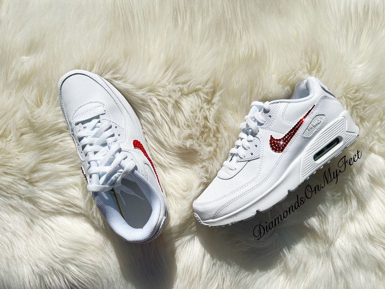 May include: White leather sneakers with a red jeweled swoosh logo. The text "Diamonds On My Feet" is visible on the right shoe.