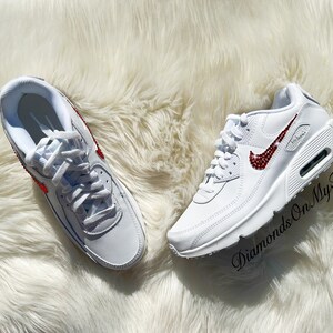 May include: White leather sneakers with a red rhinestone Nike swoosh. The shoes are on a white fluffy surface. The text "Diamonds On My Feet" is visible in the lower right corner of the image.